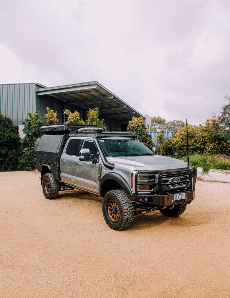 Silver Ford F-250/F-350 Super Duty with Boss cab rack and canopy parked on gravel
